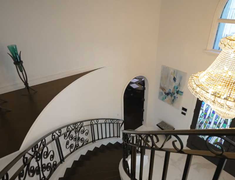 Grand foyer featuring a custom curved staircase with wrought iron railings, a crystal chandelier, and arched doorways in a luxury Vero Beach home by Island Harbor Custom Builders.