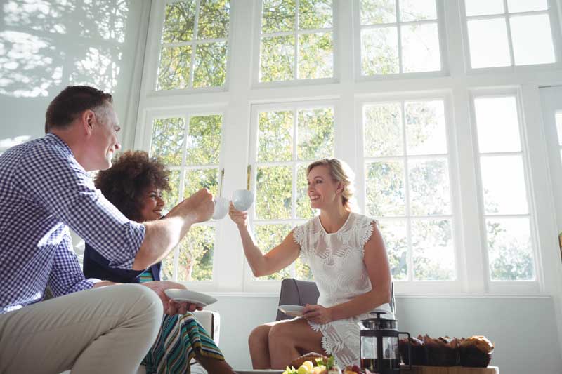 Friends enjoying coffee in a sun-filled room featuring high-end replacement windows with classic grid patterns installed by Island Harbor Custom Builders in Sebastian, FL.