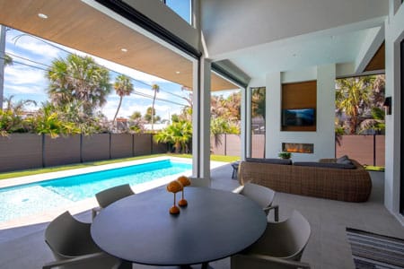 Luxury modern home in Vero Beach featuring a covered outdoor living area with linear fireplace, recessed lighting, wood-plank ceilings, and a custom lap pool by Island Harbor Custom Builders.