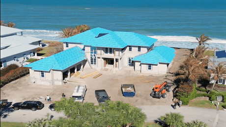 Aerial view of a luxury oceanfront custom home in Vero Beach during the dry-in phase, featuring blue roof underlayment and a large three-car garage by Island Harbor Custom Builders.