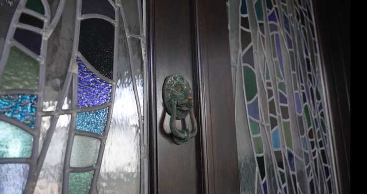 Close-up of a handcrafted stained glass entryway and antique bronze door knocker on a luxury custom home in Vero Beach, FL.
